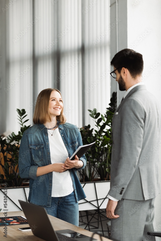 Obraz premium Smiling job seeker holding paper folder near businessman during interview in office.