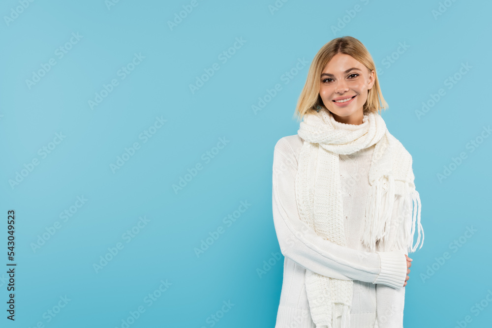 Pretty woman in warm scarf and sweater looking at camera isolated on blue.