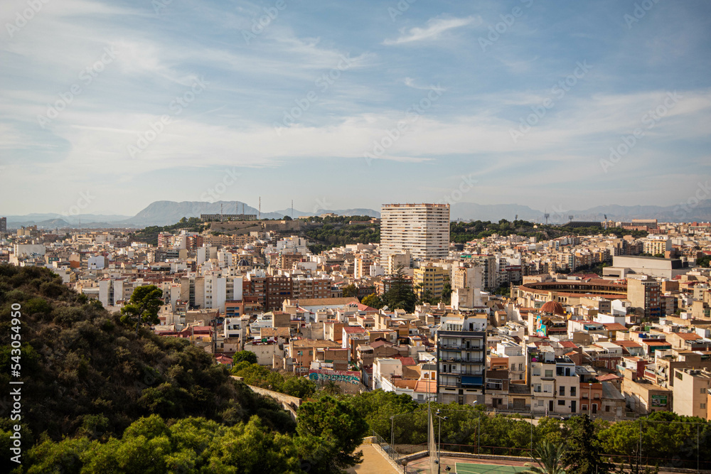 Panorámica del paisaje de la ciudad de Alicante con sus edificios y su parque bajo un cielo azul con algunas nubes en el último viaje de trabajo. 