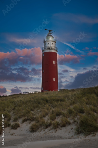 Old red lighthouse next to the dunes on Texel  Netherlands. Iconic red lighthouse in front of dark blue sky and purple clouds. Lighthouse during sunset. Typical northern sea island sunset scene.