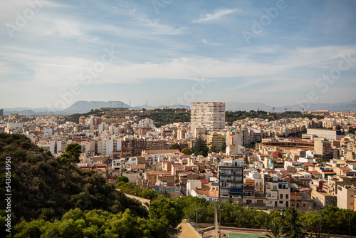 Panorámica del paisaje de la ciudad de Alicante con sus edificios y su parque bajo un cielo azul con algunas nubes en el último viaje de trabajo. 