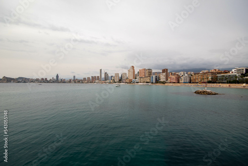 Panorámica del paisaje marítimo de la ciudad de Benidorm con su playa bajo un cielo azul con algunas nubes y el tranquilo mar en el último viaje de trabajo. 