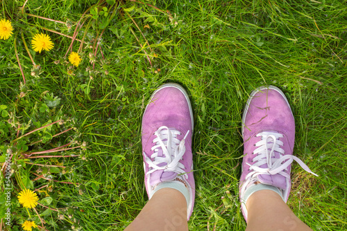 Women legs in violet sneakers on green grass