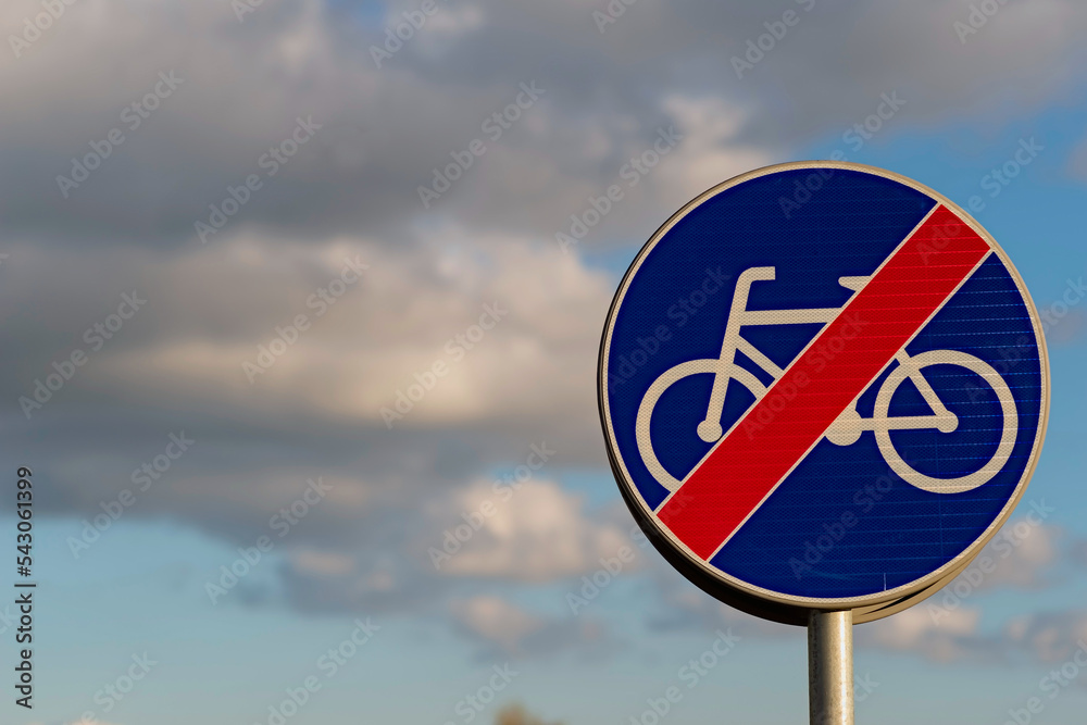 Znak drogowy : " koniec drogi dla rowerów " . Granatowy znak z przekreśloną ( białą) sylwetką roweru , na tle błękitnego nieba z białymi chmurkami .  - obrazy, fototapety, plakaty 