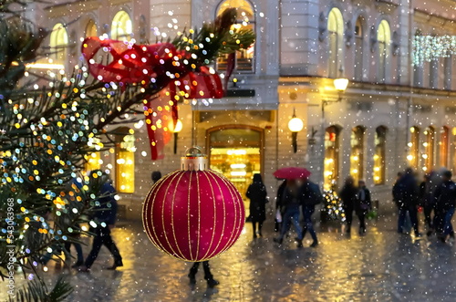  christmas red ball  festive holiday street decoration green tree branch people walk with umbrella evening blurred light medieval city Talluinn old town 