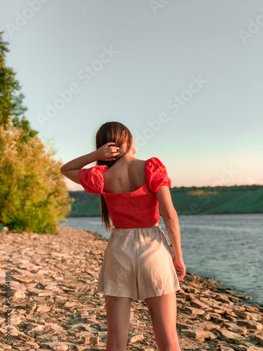 Summer girl standing near the lake, touching her hair, warm weather photo