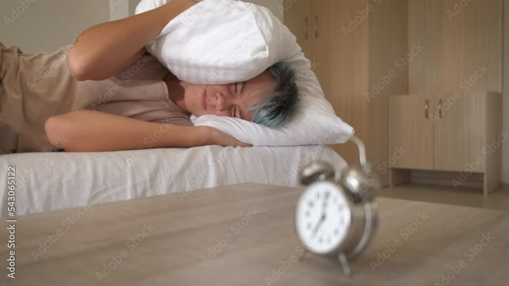 Clamps ears with a pillow in morning. A stressed teen girl clamps her