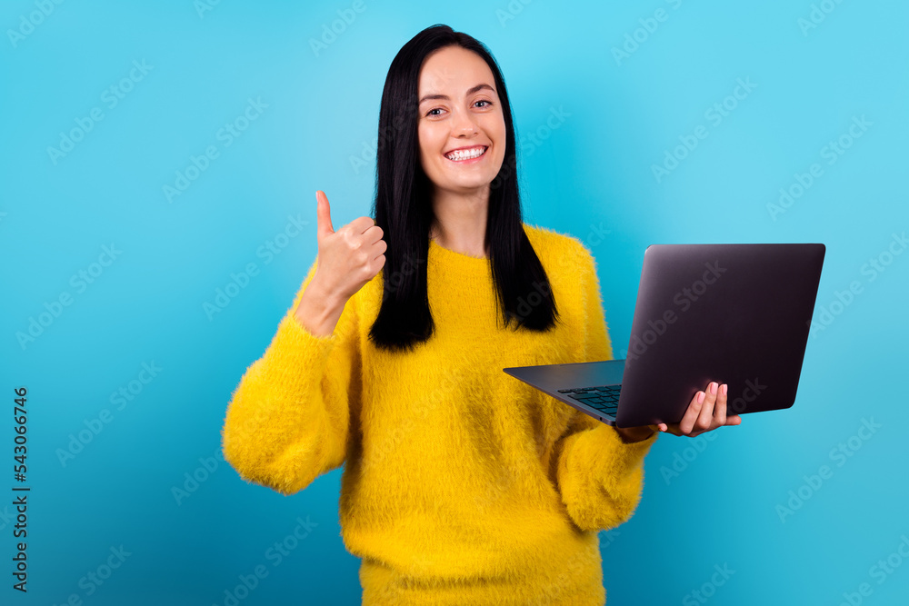 Photo portrait of cute young girl hold netbook thumb up new cool software dressed trendy yellow sweater isolated on blue color background. Photo portrait of cute young girl hold netbook thumb up new cool software dressed trendy yellow sweater isolated on blue color background.