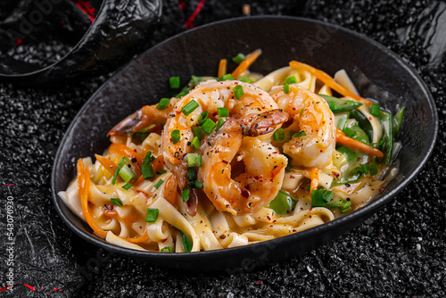 Wok shrimp in coconut milk in a plate on a black background