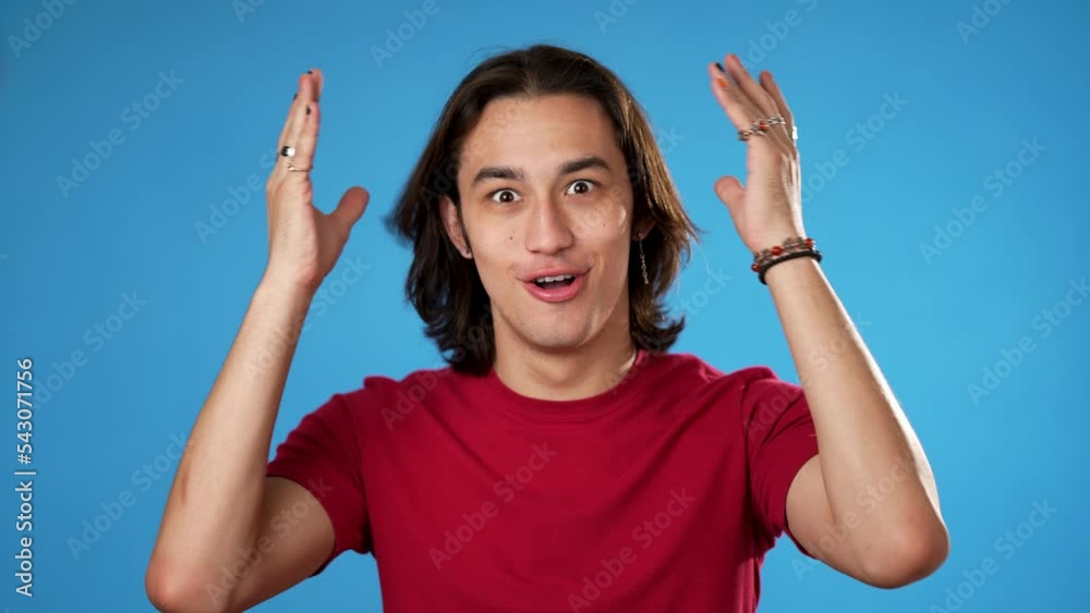 Handsome thinking gender fluid young man 20s, looks at camera gives mind blown gesture showing explosion of ideas posing on blue background.