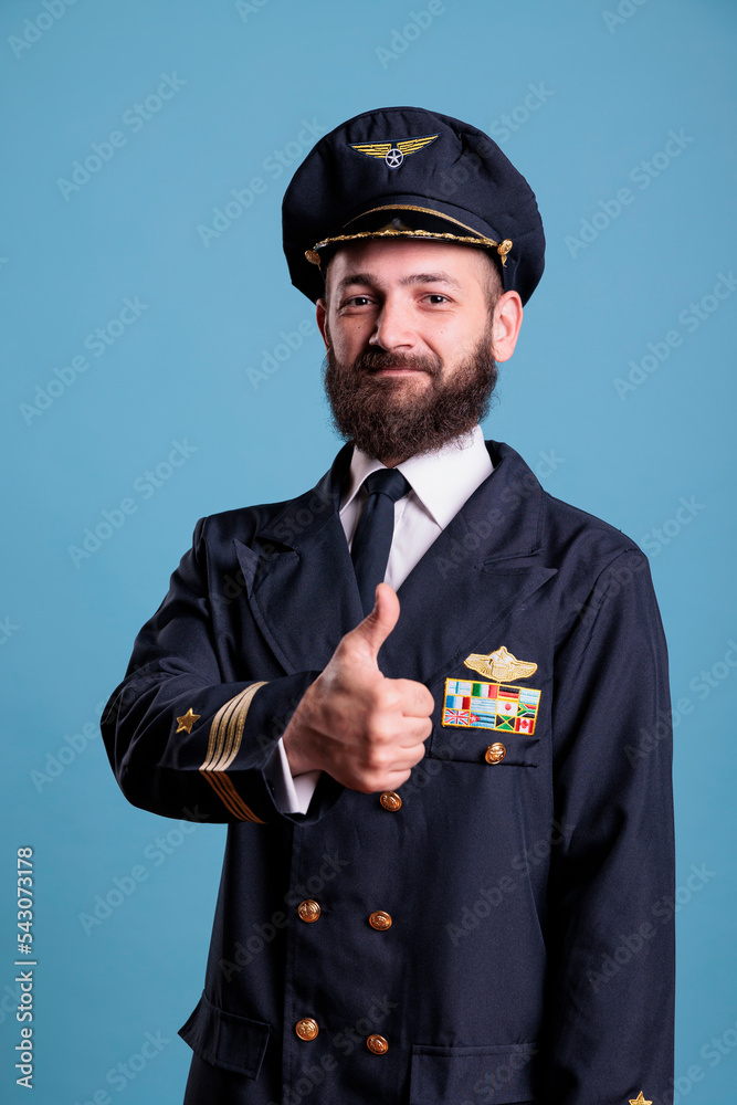 Smiling airplane aviator showing thumb up gesture wearing professional uniform portrait, plane pilot looking at camera. Aviator showing approval sign with finger, studio medium shot Smiling airplane aviator showing thumb up gesture wearing professional uniform portrait, plane pilot looking at camera. Aviator showing approval sign with finger, studio medium shot