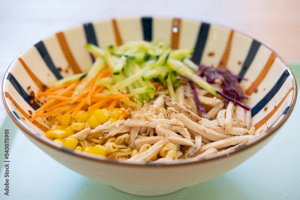 angle view bowl of cold noodles with shredded chicken and cucumber and carrot and purple cabbage