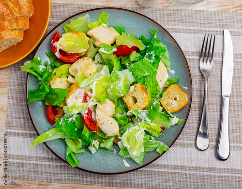 Popular dish of american cuisine is Caesar salad, made from lettuce leaves, boiled chicken breast, tomatoes, croutons and ..seasoned with sauce photo