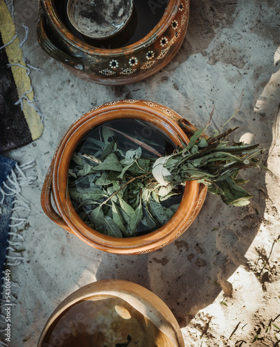 Medicinal plants macerating in ceramic jar in white sand exotic garden with golden hour light and colorful blanket during sacred ceremony in Tulum photo