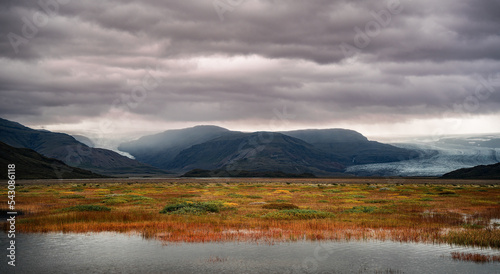panorama view of lake, tundra, mountain, glacier, sky and clouds