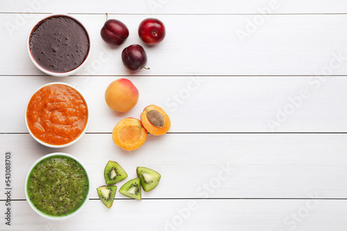 Different puree in bowls and fresh fruits on white wooden table, flat lay. Space for text