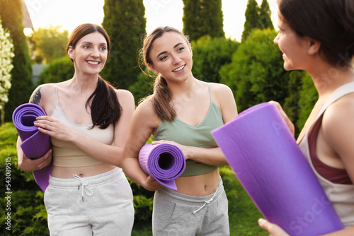 Young women in sportswear with yoga mats talking outdoors