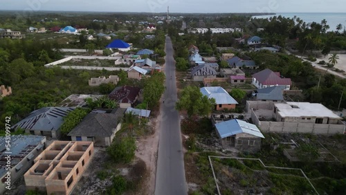 Main road across Uroa Beach town with homes under construction and people walking, Zanzibar Tanzania, Africa, Aerial flyover shot