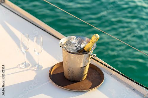 Champagne bottle in ice bucket with champagne glass on the tray for serving to passenger tourist on luxury catamaran boat yacht sailing in the ocean at sunset on summer holiday travel vacation trip. © CandyRetriever 