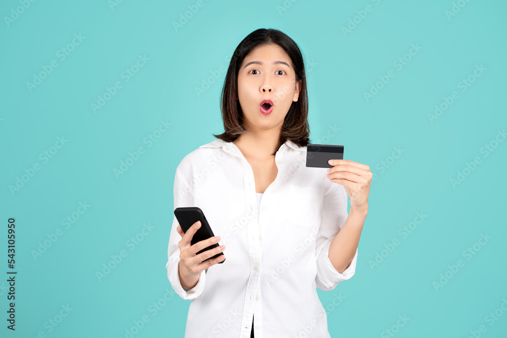 Excited and surprised young asian woman standing isolated on bright green wall background studio. She using mobile cell phone and hold credit bank card. People lifestyle concept. Excited and surprised young asian woman standing isolated on bright green wall background studio. She using mobile cell phone and hold credit bank card. People lifestyle concept.
