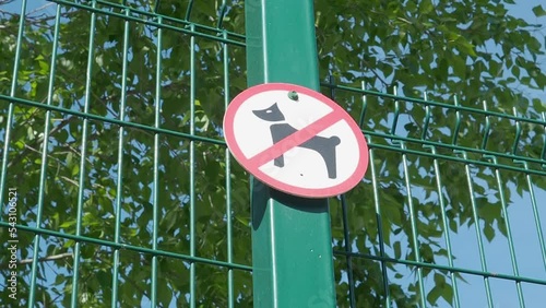 No dog walking sign on metal fence. Green leaves in the background