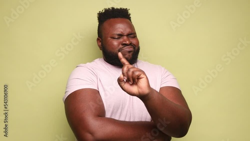 Happy funny young adult African-american man wearing pink t-shirt nodding no with head and finger, smiling with positive emotions. Indoor studio shot isolated on light green background.