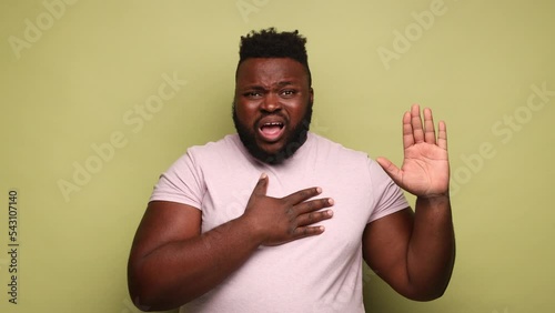 I swear. Conscious honest African-american man raising one hand and holding on chest another, swearing in honesty and devotion, patriotism. Indoor studio shot isolated on light green background.