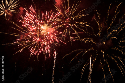 Bright fireworks with red sparks and smoke flying against the background of the night sky. Beautiful colorful festive fireworks against the black sky, long exposure. Salute background