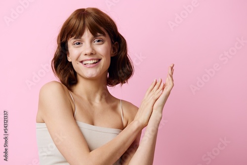 a sweet, elegant young woman stands on a pink background, happily smiling, posing with her hands in relaxed gestures. Horizontal studio photography with empty space