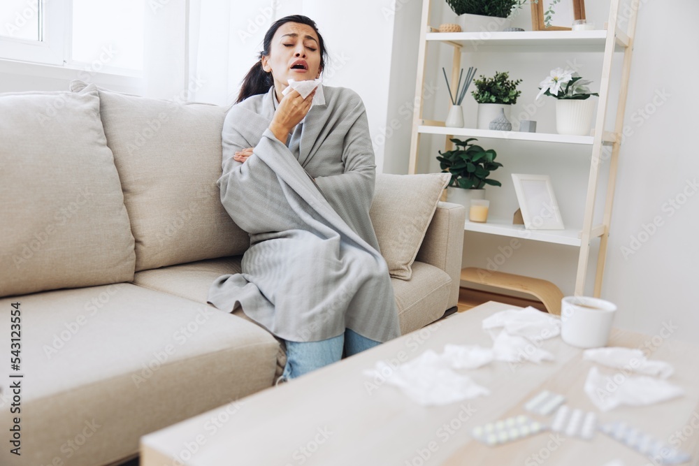 Woman cold headache runny nose and stuffy nose sitting on sofa in plaid, treatment for flu, allergies and covid-19 Woman cold headache runny nose and stuffy nose sitting on sofa in plaid, treatment for flu, allergies and covid-19