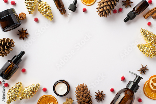 Winter skin care concept. Top view photo of amber bottles christmas decor golden pine cone ornaments mistletoe berries dried citrus slices on isolated white background with copyspace in the middle