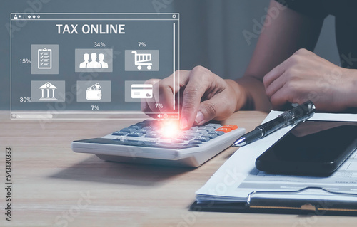 Business people hand using calculator calculate refund tax of duty taxation business with bar TAX ONLINE, graphs and chart being demonstrated on the screen media and selecting tax refund.