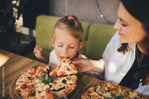 Mother and daughter eat pizza in a cafe.