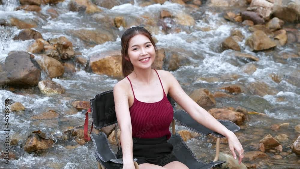 Asian woman in red sitting on a chair with big rocks and water slow splashing for relaxing and happiness in the vacation summertime Asian woman in red sitting on a chair with big rocks and water slow splashing for relaxing and happiness in the vacation summertime