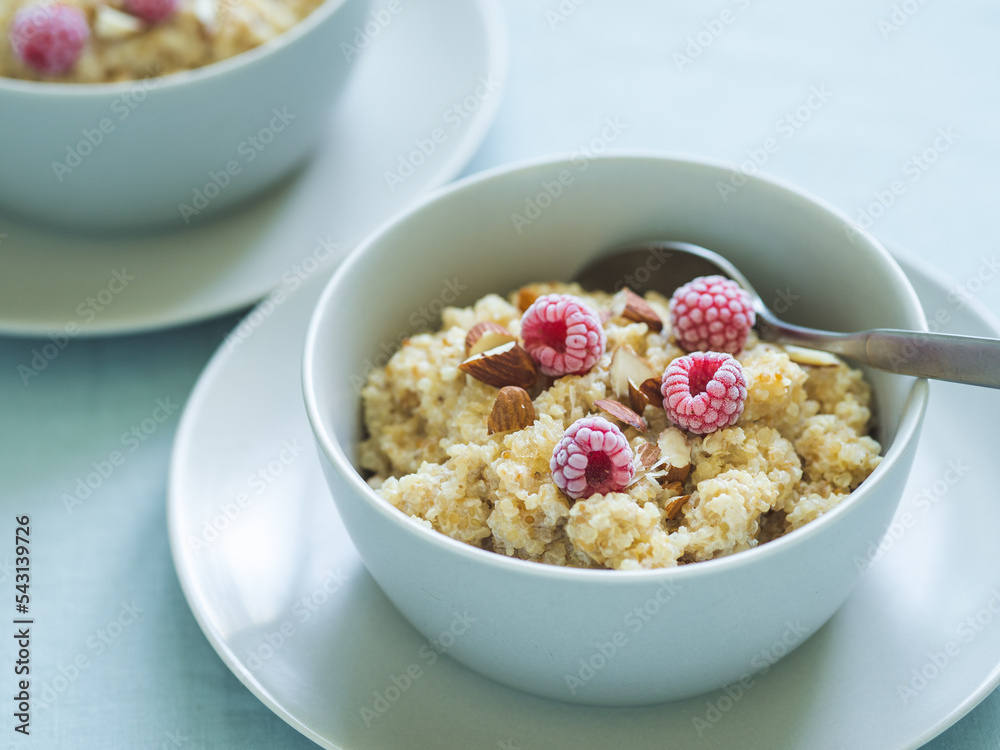 Quinoa porrige on tabletop. Two bowl wit quinoa milk porridge with berries and almond. Frozen raspberries in quinoa porrige Quinoa porrige on tabletop. Two bowl wit quinoa milk porridge with berries and almond. Frozen raspberries in quinoa porrige