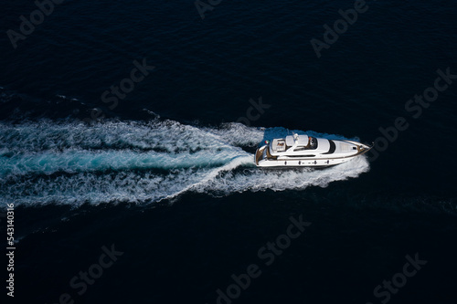 A large expensive yacht is moving fast on dark water in the rays of the sun top view. White yacht fast movement on dark water air view. © Berg