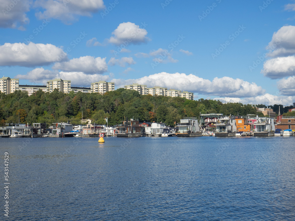 Row of houseboats overlooked by apartment buildings with trees in between  in summer