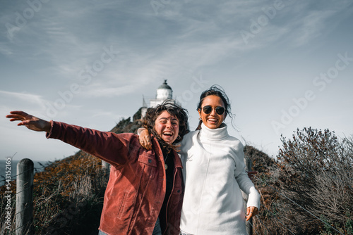 two caucasian tousled happy happy girls jumping and running looking at camera on narrow dirt road coming from lighthouse, nugget point, new zealand photo