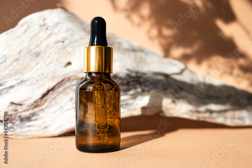 Glass bottle with an amber-colored pipette with facial serum on a natural dry wood background