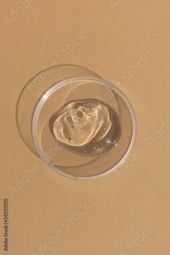 Hyaluronic acid serum or gel for the face in Petri dish on a beige background. Concept of cosmetics laboratory researches, wellness and beauty. Cosmetic texture. Top view