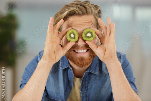 Fotografia comical image of man covering eyes with kiwi slices