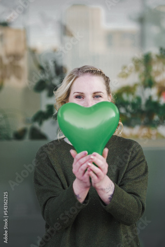 smiling young vegan girl full of joy holding a green heart air balloon in her hand for more environmentally friendly awareness to care about planet earth against climate change 
