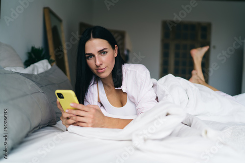 Young woman lying on bed using smartphone photo