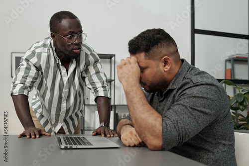 Angry African American businessman rebuking his colleague or subordinate of another ethnicity networking by workplace photo