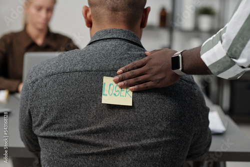 Tablou pe pânză Hand of black man putting sticker with written word loser on back of colleague w