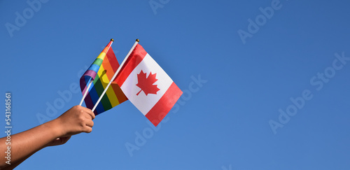 Canadian national flag and rainbow flag holding in hands against bluesky backgrouhd, soft and selective focus, concept for lgbt gender celebration in pride month around the world. photo