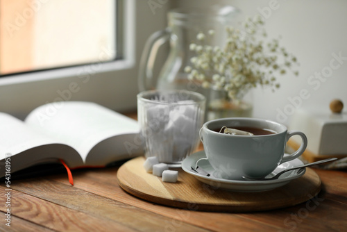 Tray with cup of freshly brewed tea and sugar cubes on wooden table  space for text