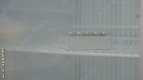 Close Up Of Scientist In Blue Gloves Placing Vials With Laboratory Samples Onto Fridge Shelf For Storage, 4K photo