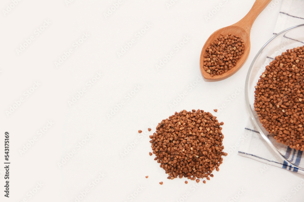 small grains of natural brown buckwheat in a wooden spoon and a glass plate small grains of natural brown buckwheat in a wooden spoon and a glass plate