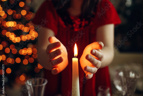 dark, atmospheric, christmas photo, candle burning, children's hands nearby, girl's hands, christmas lights, garland in the background